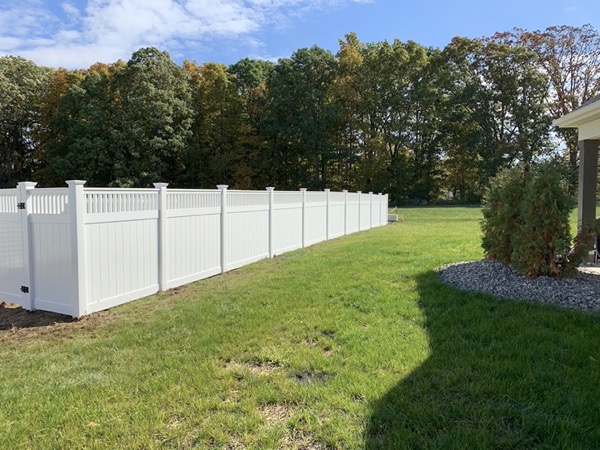 A white vinyl privacy fence run under a blue sky